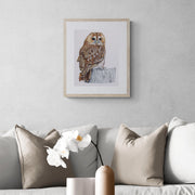 Greenwich Owl limited edition embroidery art print by Susannah Weiland, shown framed in natural wood with a white mount and hung on a grey textured wall above a neutral linen sofa in a contemporary interior.