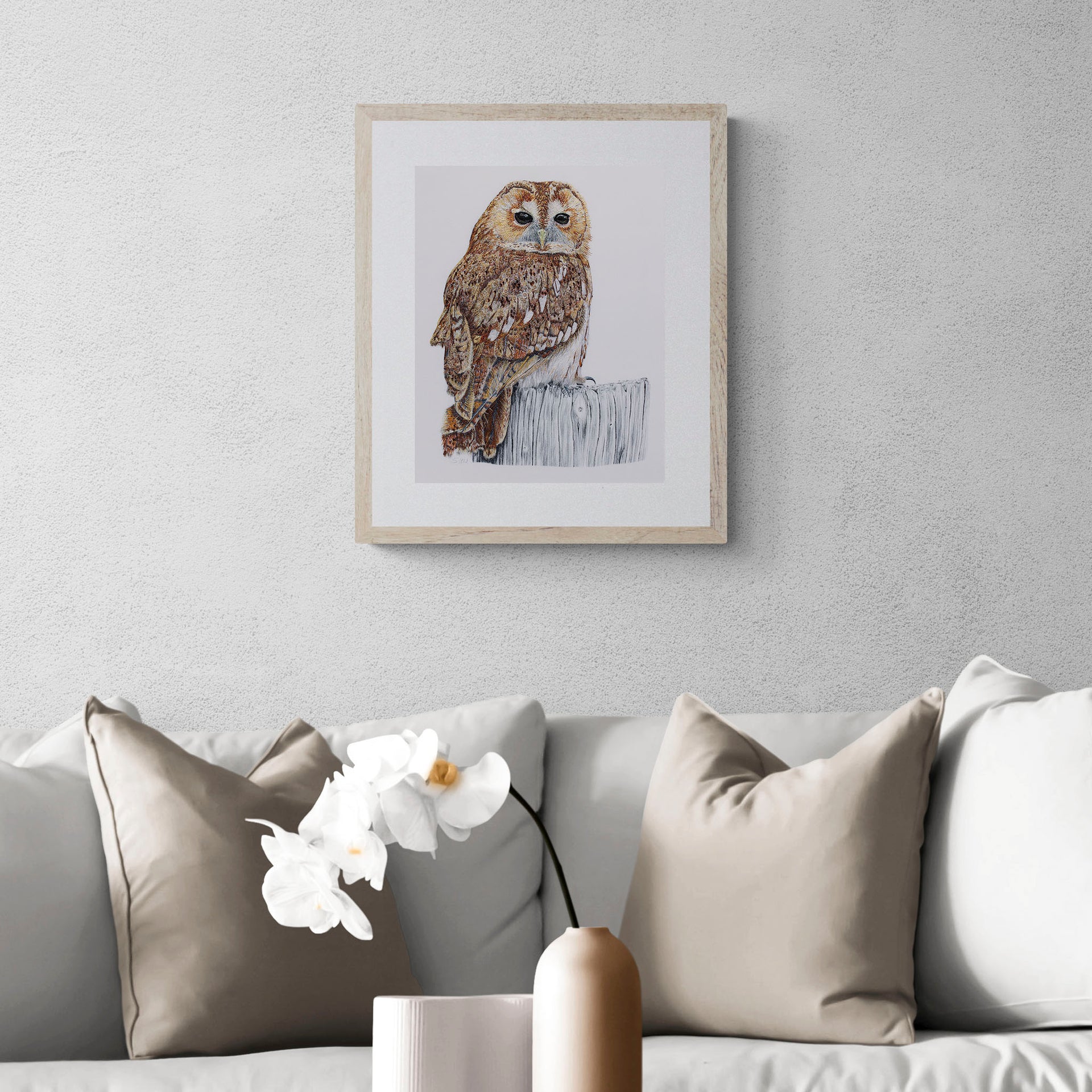 Greenwich Owl limited edition embroidery art print by Susannah Weiland, shown framed in natural wood with a white mount and hung on a grey textured wall above a neutral linen sofa in a contemporary interior.