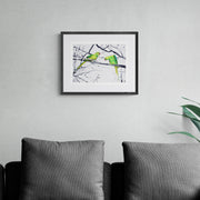 Hyde Park Parakeets limited edition embroidery art print by Susannah Weiland, shown in a dark frame with white mount above a charcoal sofa, the vivid greens of the parakeets striking against a grey interior palette.